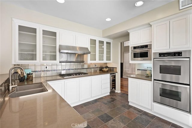 kitchen with sink, appliances with stainless steel finishes, white cabinetry, wine cooler, and tasteful backsplash