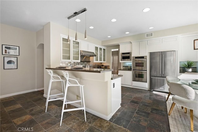 kitchen featuring decorative light fixtures, appliances with stainless steel finishes, kitchen peninsula, decorative backsplash, and white cabinets