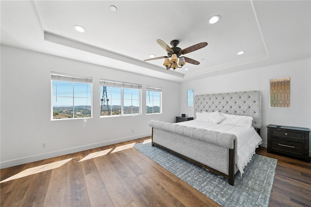 bedroom with ceiling fan, a tray ceiling, and dark hardwood / wood-style flooring