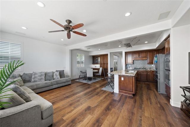 kitchen featuring tasteful backsplash, ceiling fan, dark hardwood / wood-style floors, a kitchen island, and light stone countertops