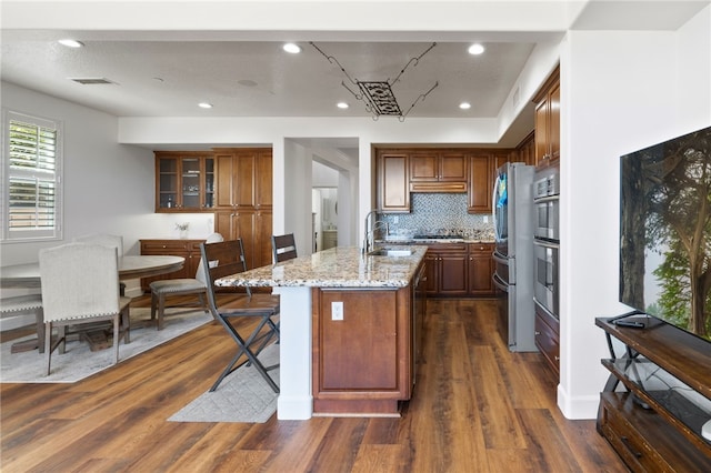 kitchen featuring light stone countertops, stainless steel appliances, an island with sink, sink, and dark hardwood / wood-style floors