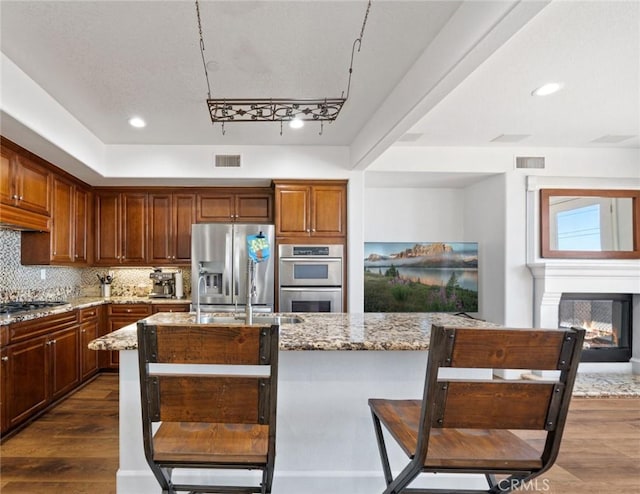 kitchen featuring light stone countertops, dark hardwood / wood-style flooring, stainless steel appliances, a multi sided fireplace, and backsplash