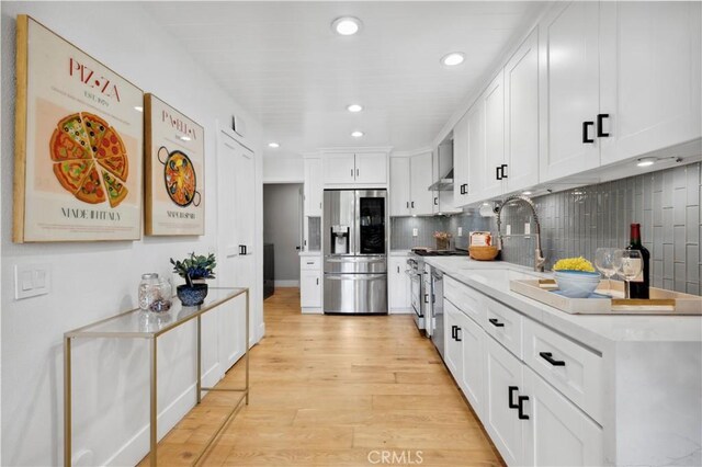 kitchen featuring white cabinetry, sink, backsplash, appliances with stainless steel finishes, and light wood-type flooring