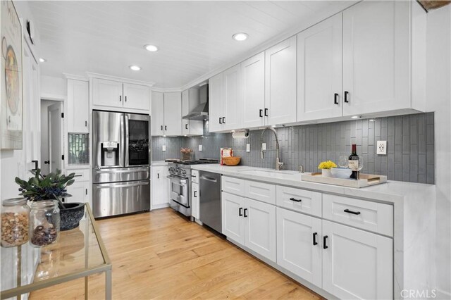 kitchen with wall chimney exhaust hood, stainless steel appliances, sink, light hardwood / wood-style flooring, and white cabinets