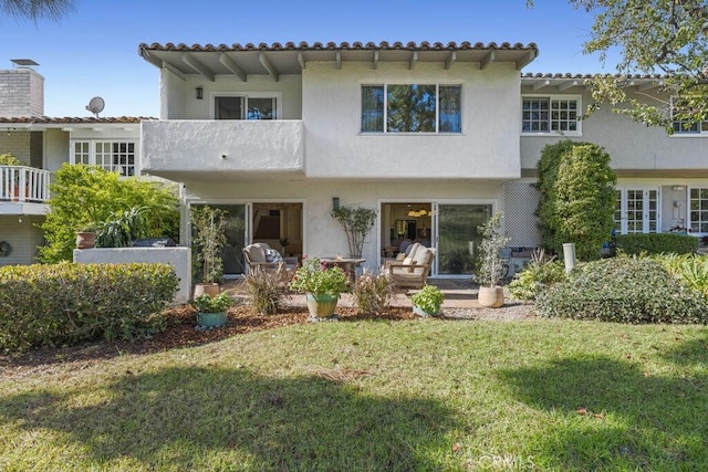 rear view of house featuring a balcony, stucco siding, a patio, and a yard