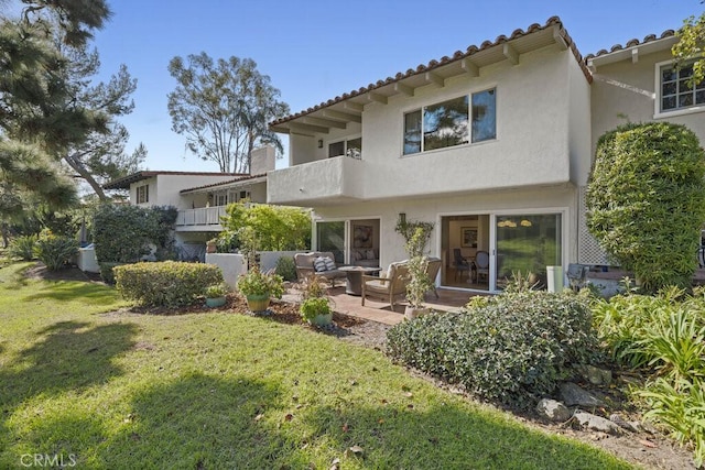 view of front facade featuring a patio, stucco siding, a front yard, a balcony, and a tiled roof