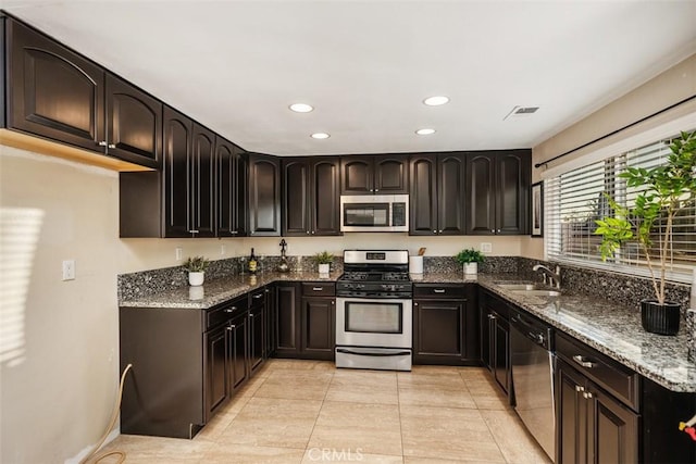 kitchen featuring dark stone counters, sink, light tile patterned floors, and stainless steel appliances