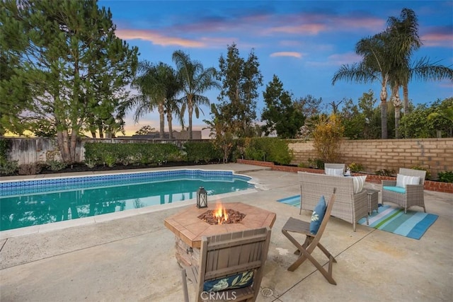 pool at dusk with an outdoor living space with a fire pit and a patio area