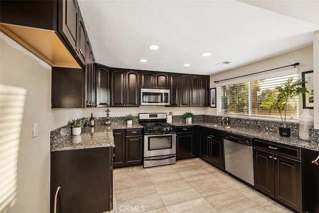 kitchen featuring appliances with stainless steel finishes, dark brown cabinetry, dark stone counters, and sink