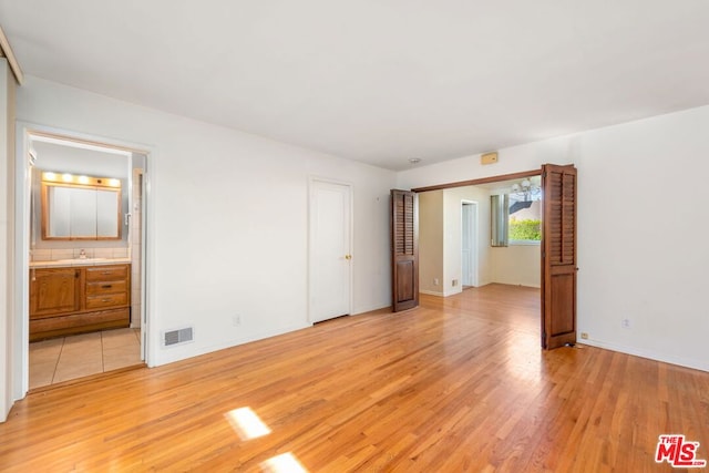 unfurnished bedroom with ensuite bath, sink, and light wood-type flooring