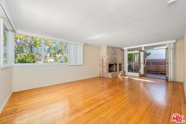 unfurnished living room with light wood-type flooring, a stone fireplace, and plenty of natural light