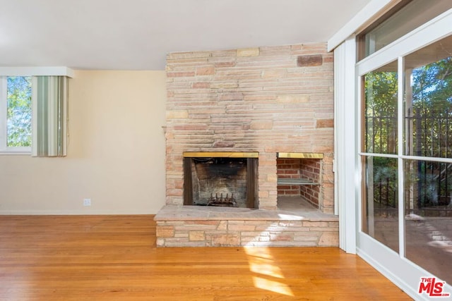 unfurnished living room featuring hardwood / wood-style floors, plenty of natural light, and a stone fireplace