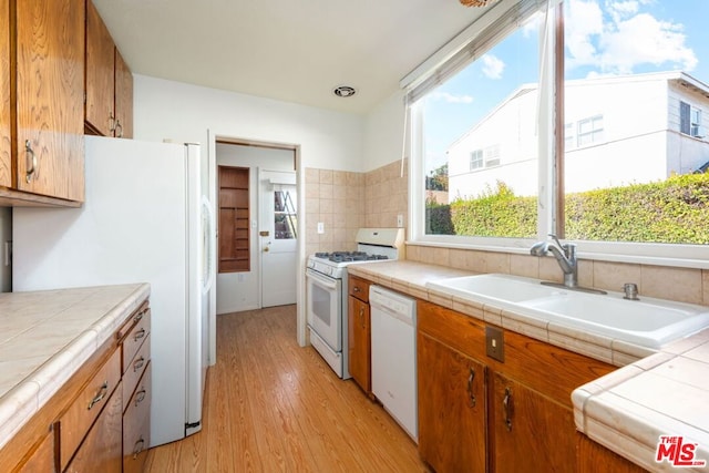 kitchen featuring light wood-type flooring, backsplash, white appliances, sink, and tile counters