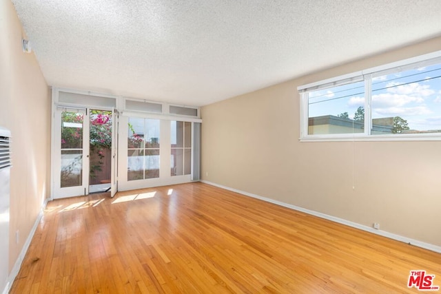 unfurnished room featuring french doors, a textured ceiling, light hardwood / wood-style floors, and a healthy amount of sunlight