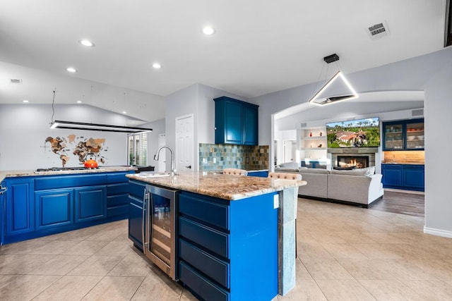 kitchen with a kitchen island with sink, blue cabinets, sink, light stone countertops, and beverage cooler