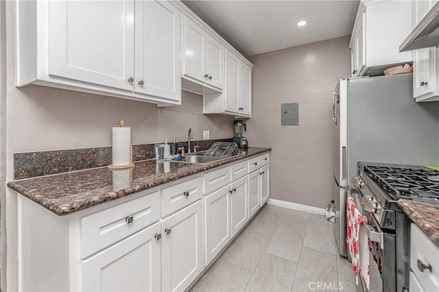 kitchen with dark stone counters, extractor fan, high end stainless steel range oven, sink, and white cabinetry