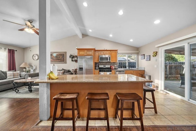 kitchen with vaulted ceiling with beams, a kitchen bar, decorative backsplash, stainless steel appliances, and light wood-type flooring