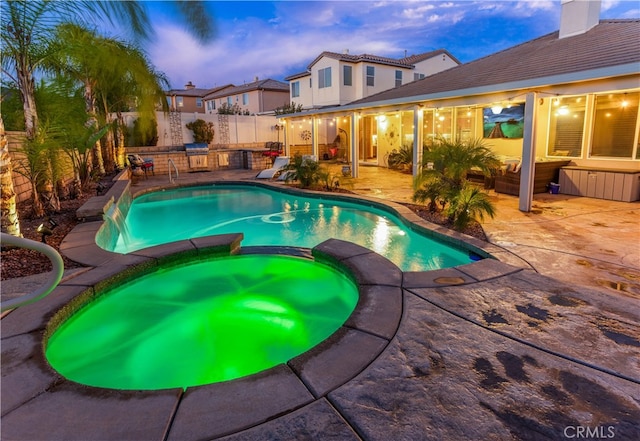 pool at dusk featuring a patio area, an in ground hot tub, and an outdoor kitchen