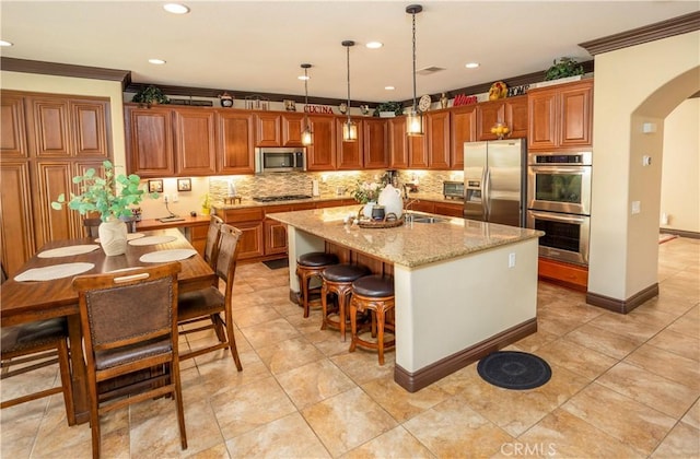 kitchen featuring light stone countertops, hanging light fixtures, crown molding, a center island with sink, and appliances with stainless steel finishes