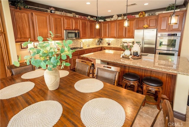 kitchen with hanging light fixtures, light stone countertops, ornamental molding, tasteful backsplash, and stainless steel appliances