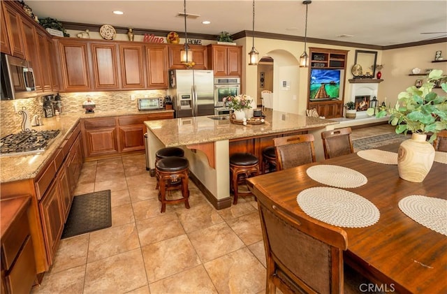 kitchen featuring a center island, light stone counters, crown molding, decorative light fixtures, and appliances with stainless steel finishes