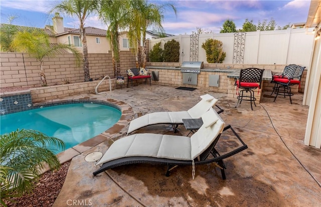 pool at dusk featuring an outdoor kitchen and a grill