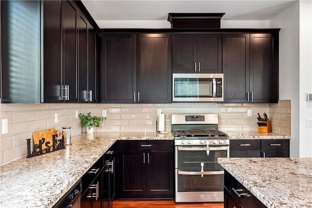 kitchen with tasteful backsplash, light stone counters, wood-type flooring, dark brown cabinets, and appliances with stainless steel finishes