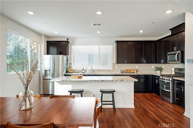 kitchen with light stone counters, dark hardwood / wood-style flooring, a kitchen island, and stainless steel appliances