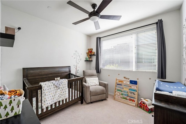 bedroom with ceiling fan, a nursery area, and light carpet