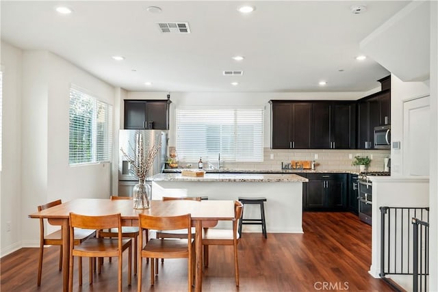 kitchen featuring light stone countertops, decorative backsplash, dark hardwood / wood-style flooring, stainless steel appliances, and a center island