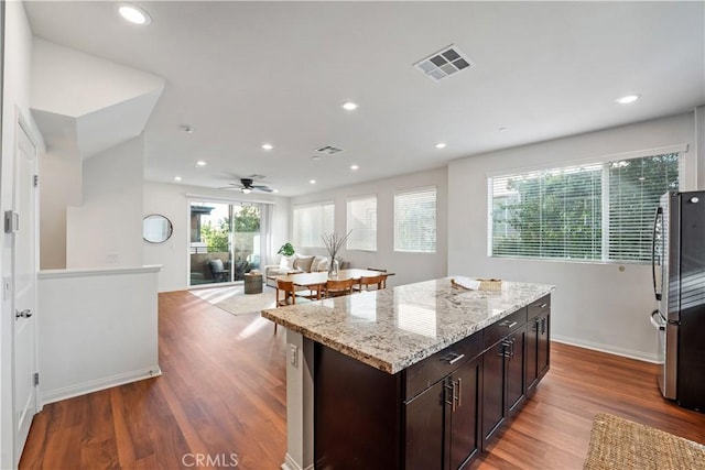 kitchen with ceiling fan, a kitchen island, wood-type flooring, and stainless steel refrigerator