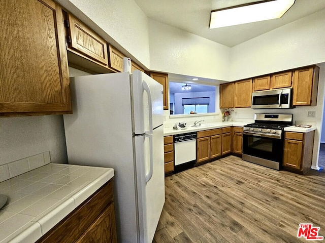 kitchen with tile countertops, light hardwood / wood-style flooring, stainless steel appliances, and sink