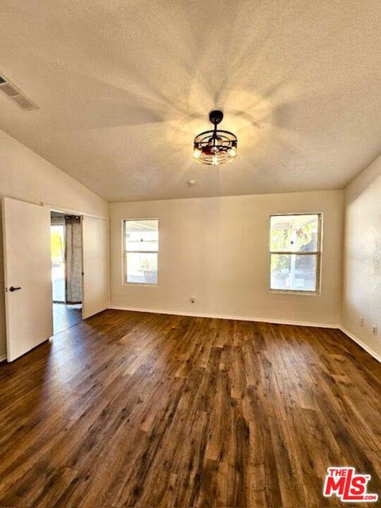 unfurnished room featuring dark hardwood / wood-style flooring, a textured ceiling, and vaulted ceiling