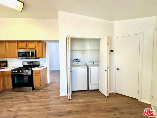 kitchen featuring washer and dryer, light hardwood / wood-style floors, and appliances with stainless steel finishes