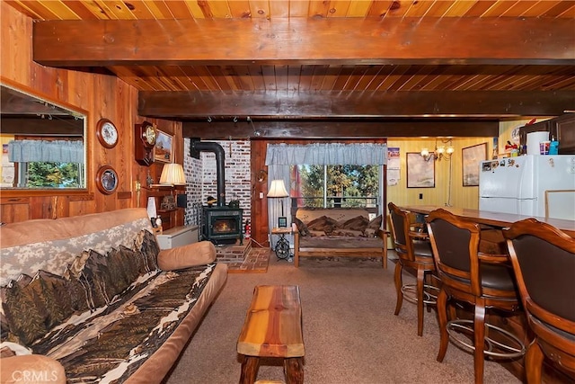 living room featuring a wood stove, an inviting chandelier, wooden walls, beam ceiling, and wood ceiling