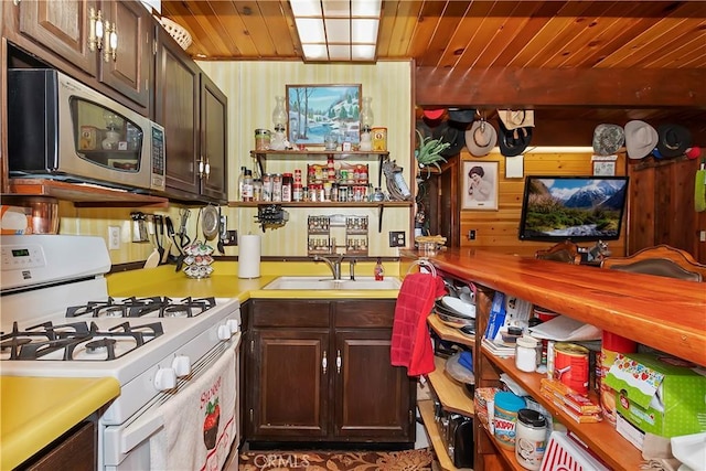 kitchen with sink, white range with gas cooktop, wooden walls, dark brown cabinets, and wood ceiling