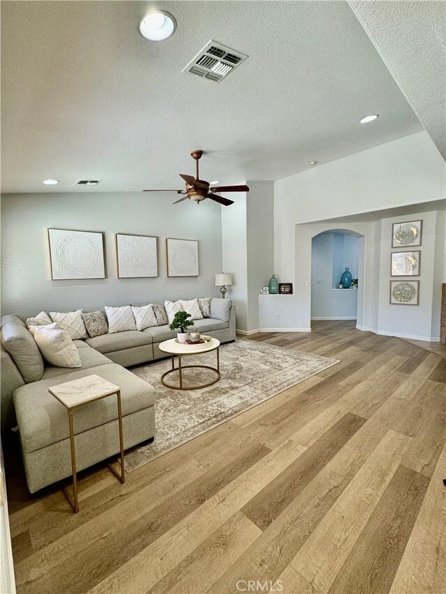 living area featuring arched walkways, visible vents, a textured ceiling, and wood finished floors