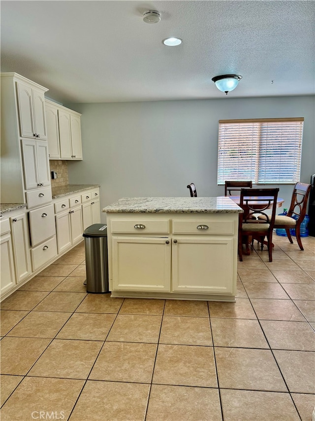 kitchen featuring white cabinets, a kitchen island, light stone countertops, and light tile patterned floors