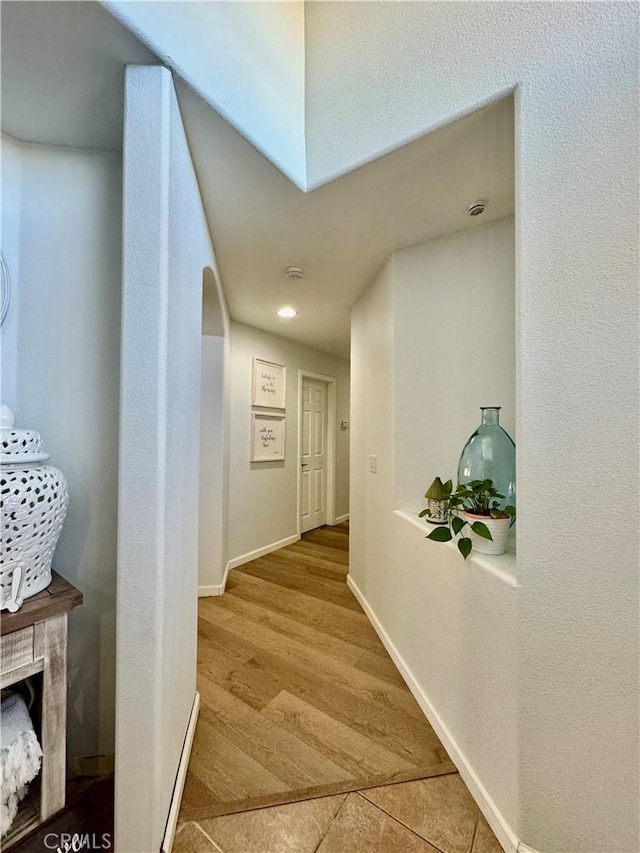 hall featuring arched walkways, baseboards, and wood finished floors