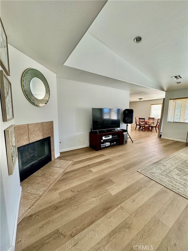 living room featuring vaulted ceiling, a tiled fireplace, light hardwood / wood-style floors, and a textured ceiling