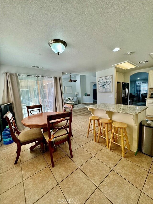 dining room with light tile patterned floors, arched walkways, visible vents, and a ceiling fan