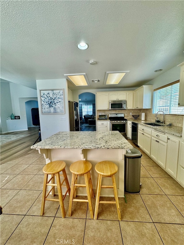 kitchen featuring light stone countertops, sink, a kitchen bar, a kitchen island, and appliances with stainless steel finishes