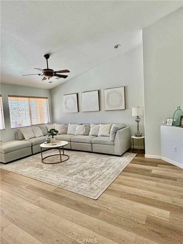 living room featuring ceiling fan, vaulted ceiling, a textured ceiling, and light hardwood / wood-style flooring