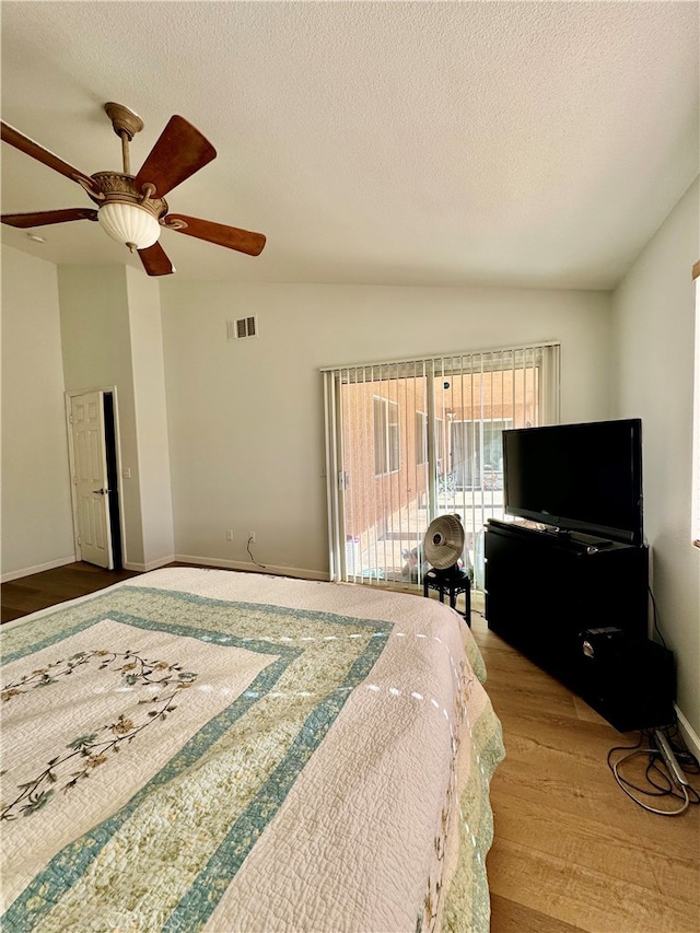 bedroom with a textured ceiling, light hardwood / wood-style flooring, ceiling fan, and vaulted ceiling