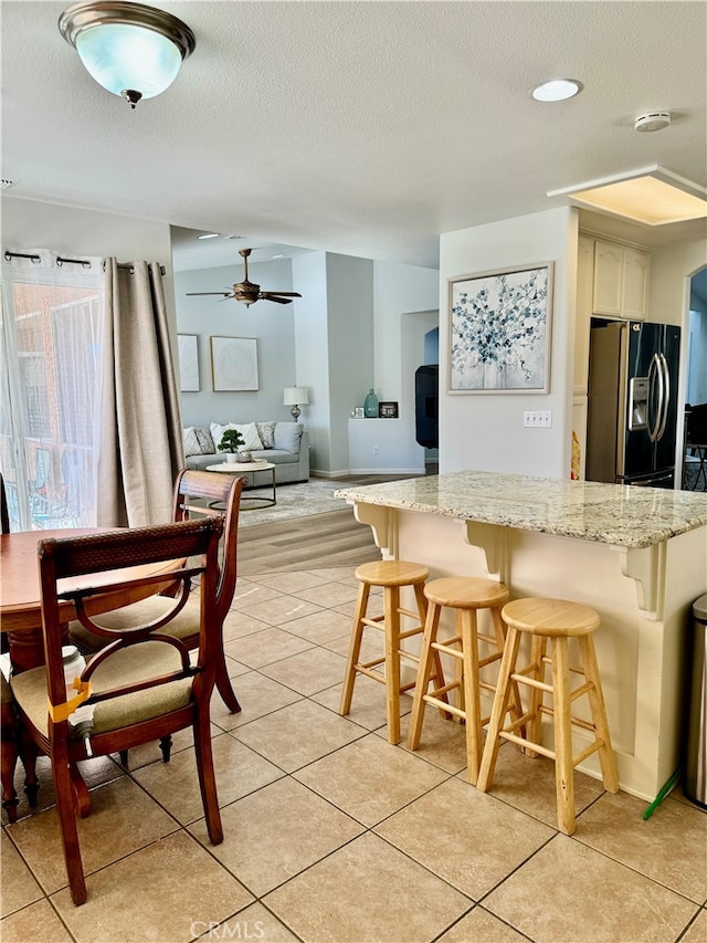 kitchen featuring stainless steel refrigerator with ice dispenser, a textured ceiling, light tile patterned floors, and a breakfast bar area