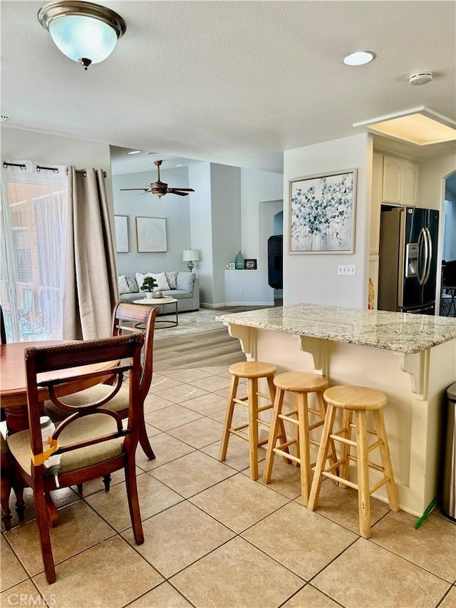 kitchen with light stone counters, a breakfast bar, a textured ceiling, black fridge, and light tile patterned flooring