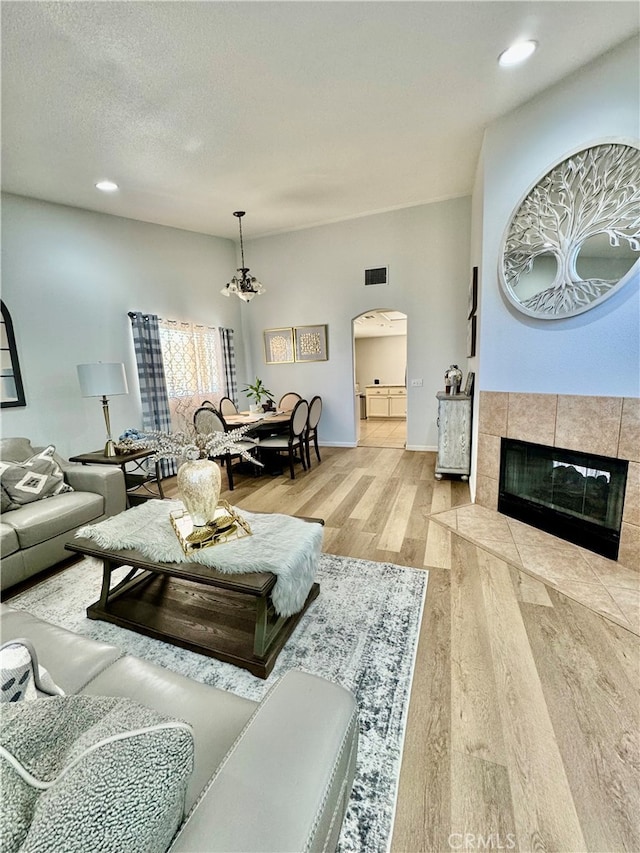 living room featuring a tile fireplace, a textured ceiling, light hardwood / wood-style floors, and a notable chandelier