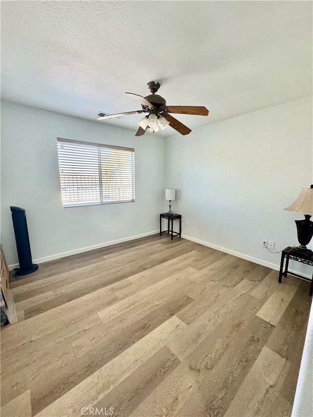 empty room featuring ceiling fan, a textured ceiling, baseboards, and wood finished floors