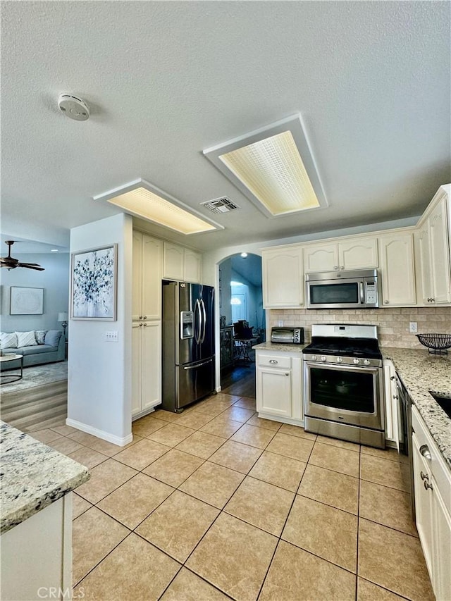 kitchen with arched walkways, light tile patterned floors, stainless steel appliances, visible vents, and backsplash