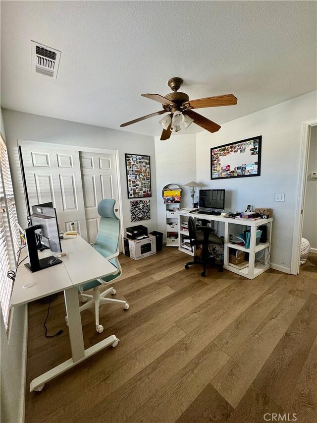 home office with ceiling fan, a textured ceiling, visible vents, and wood finished floors